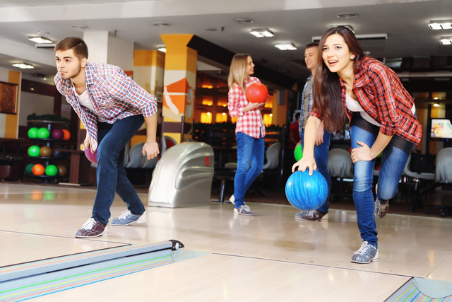 Ein Mann und eine Frau sind gemeinsam beim Bowlen – beide sind gerade dabei, ihre Kugel auf die Bahn zu werfen.