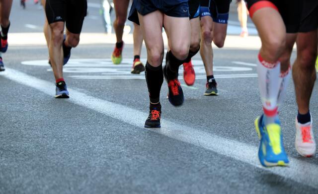 Zu sehen sind Beine in kruzen Hosen und Sportschuhen beim Rennen auf Asphalt.