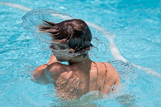 Ein junger Mann von oben fotografiert, während er im Schwimmbad schwimmt – das Wasser glitzert um ihn herum.